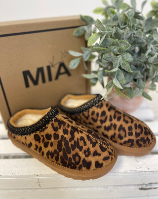 Leopard print slippers with black trim on a white surface next to a plant and 'MIA' branded box.