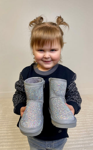Gray children's boots with rhinestone details on a wooden surface with a plant and MIA Kids