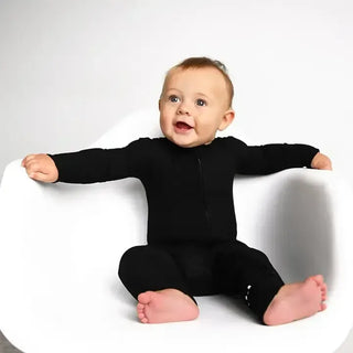 Baby wearing a black onesie sitting on a white chair against a white background