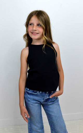 Young girl wearing a black sleeveless top and blue jeans against a white background