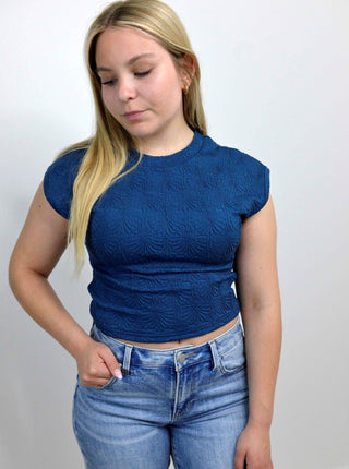 woman wearing a cap sleeve fitted waist length blue top