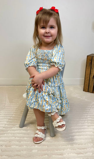 Young girl in a floral dress sitting on a stool with a white background