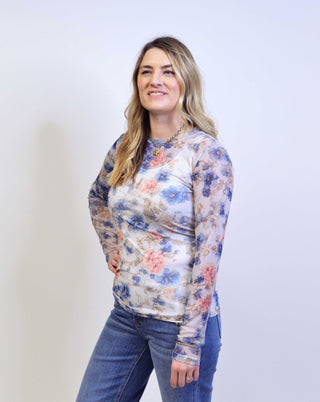 Woman wearing a floral long-sleeve top and jeans against a plain background
