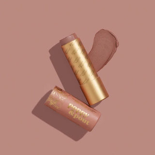 A lip balm stick and its cap arranged diagonally on a dusty rose background, with a smear of the balm showing the shade. The packaging is metallic gold and dusty rose pink with 'poppy & pout' printed in gold.