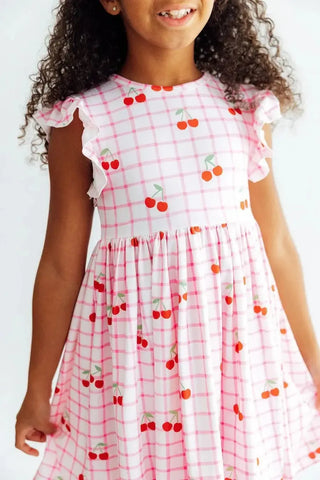 Young girl wearing a pink checkered dress with cherry pattern against a white background