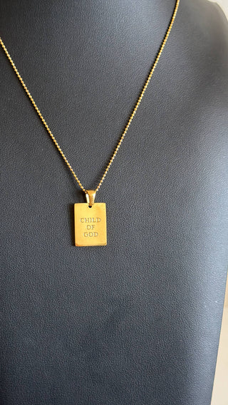 A gold rectangular pendant necklace engraved with 'CHILD OF GOD' on a textured black display bust.
