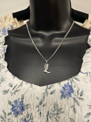 Silver necklace with a cowboy boot pendant on a mannequin wearing a floral dress.