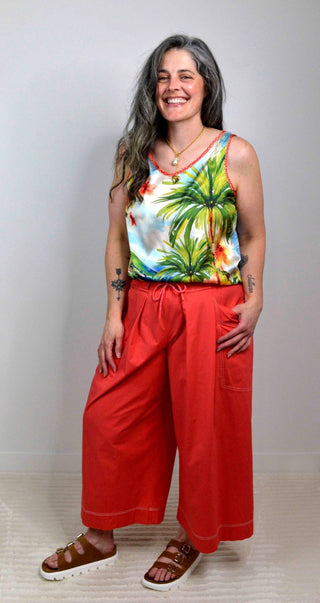 Woman wearing a colorful tropical print top and red pants against a plain background