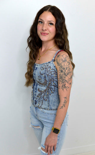 Woman wearing a denim tank top with floral patterns against a white background