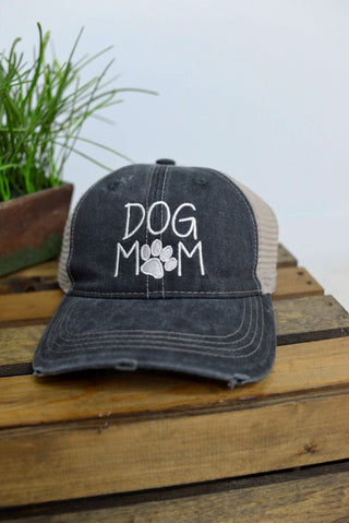 Black cap with 'DOG MOM' text on a wooden surface with a plant in the background