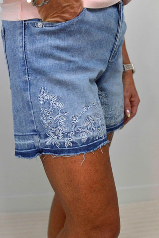 Blue denim shorts with floral embroidery on a plain background