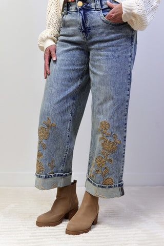 Person wearing blue jeans with floral embroidery and brown boots on a white background