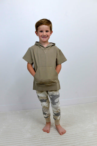 Child wearing a green hoodie and camouflage pants standing on a white background