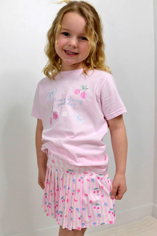 Young girl wearing a pink t-shirt and skirt with floral patterns against a white background