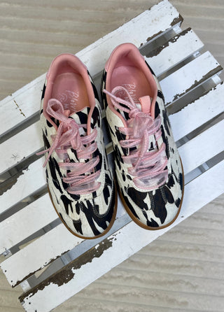 Pair of black and white patterned sneakers with pink laces on a wooden surface
