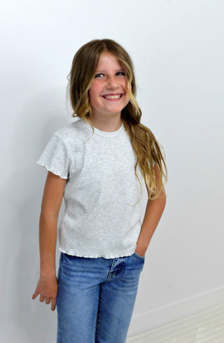 Young girl wearing a grey shirt and blue jeans against a plain background