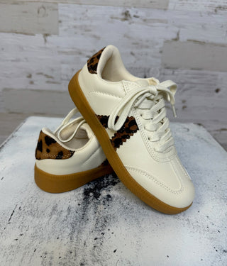 White sneakers with brown soles and leopard print accents on a textured surface.