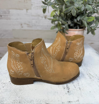 Pair of girls tan boots with decorative stitching on a light surface with a plant in the background