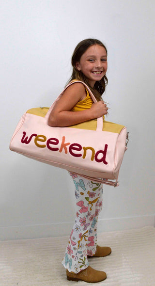 Girl holding a large pink bag with 'weekend' written on it against a white background