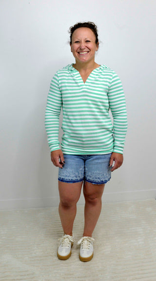 Person wearing a green and white striped shirt with denim shorts on a plain background