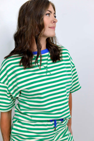 A woman wearing a green and white horizontally striped short-sleeve top with a blue collar and matching green-and-white striped bottoms, photographed against a plain light background.