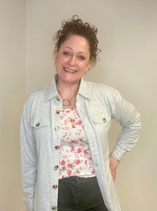 Woman wearing a light gray button down over a floral shirt with a plain background