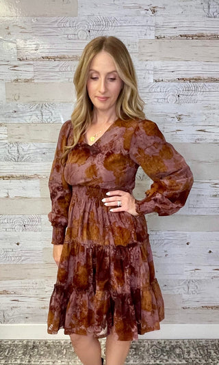 Woman wearing a brown patterned dress against a wooden panel background