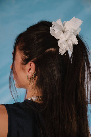A hair accessory featuring a large white ruffled fabric bow with delicate lace trim, styled in a ponytail on a model against a blue background.