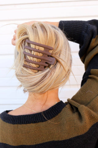 Person with a large brown hair clip in their blonde hair against a white background