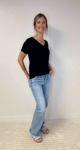 Woman wearing a black t-shirt and blue jeans standing against a white wall.