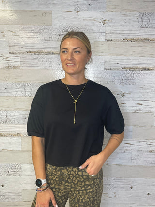 Woman wearing a black top and patterned pants standing against a wooden wall.