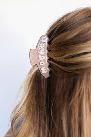 Hair clip with 'mother' text on a person's hair against a white background
