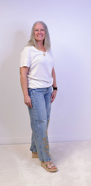 Person wearing a oatmeal t-shirt and blue jeans standing against a plain background