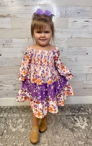 Child wearing a floral dress with purple accents against a wooden panel background