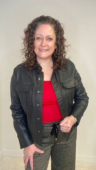 Woman wearing a black jacket over a red top with a neutral background
