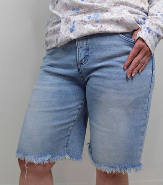 Person wearing light blue denim shorts with a floral top against a plain background
