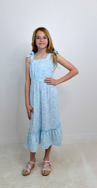 Young girl wearing a light blue dress with ruffled hem on a white background