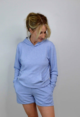 Woman wearing a light blue hoodie and shorts set against a plain background