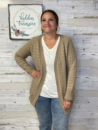Woman wearing a beige cardigan over a white shirt with a wooden floor background