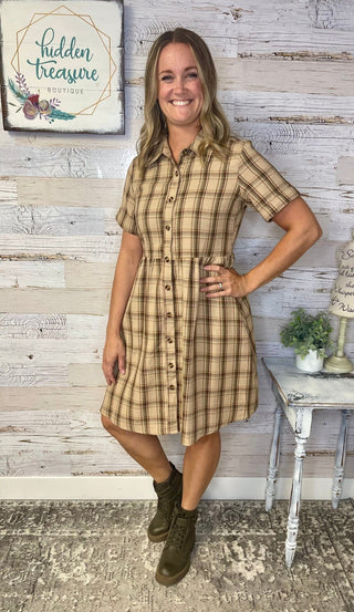Woman wearing a plaid dress standing in front of a wooden wall with 'Hidden Treasure' sign.
