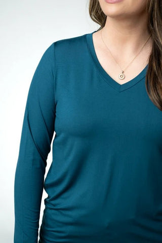 A close-up of a woman wearing a teal blue long-sleeve V-neck top, showing the chest, neckline, and part of her hair and a delicate necklace.