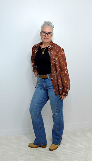 Person wearing a western patterned shirt, black top, blue jeans, and brown shoes against a white background