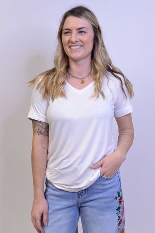 Woman wearing a white t-shirt and blue jeans with floral pants, standing against a plain background.