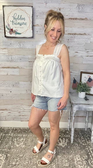 Woman wearing a white sleeveless top and denim shorts standing in a room with wooden walls and decor.