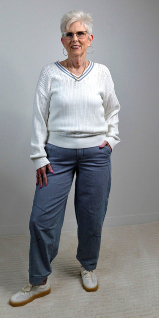 Woman wearing a white sweater and blue pants standing against a plain background
