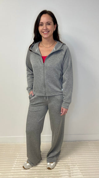 Woman wearing a gray tracksuit standing against a white wall.