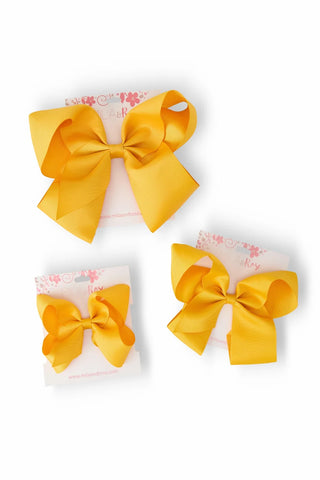 Three yellow satin hair bows of different sizes displayed on their white backing cards against a white background.